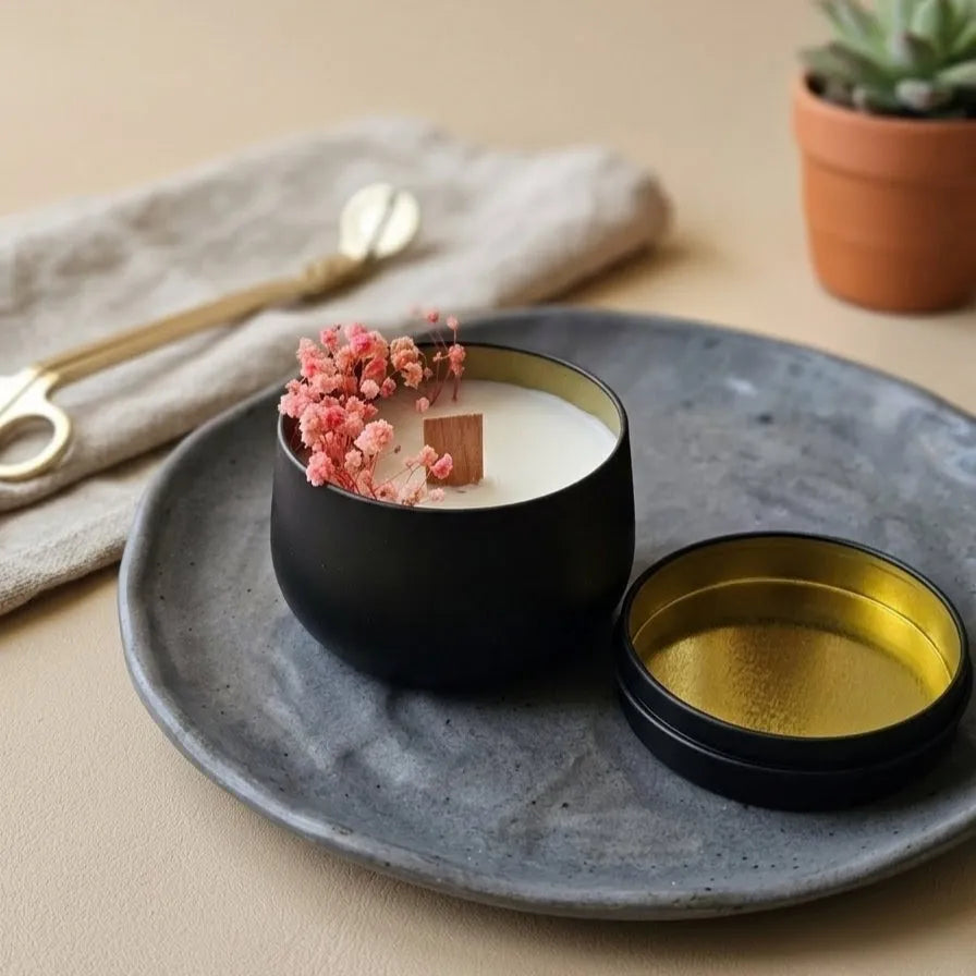 A high-contrast top-down view of the black tin candle, highlighting the intricate details of the real dried flower petals embedded in the clean white wax