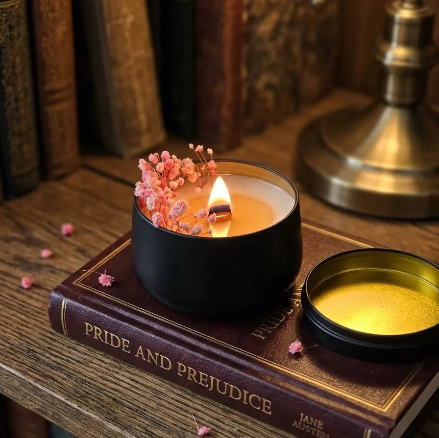 A lit round black tin candle burning cleanly with a warm, steady flame, softly illuminating the dried flower decoration inside