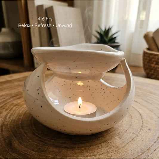 A white ceramic diffuser lit by a warm tealight candle inside, casting soft shadows while melting an aromatherapy wax sachet on top